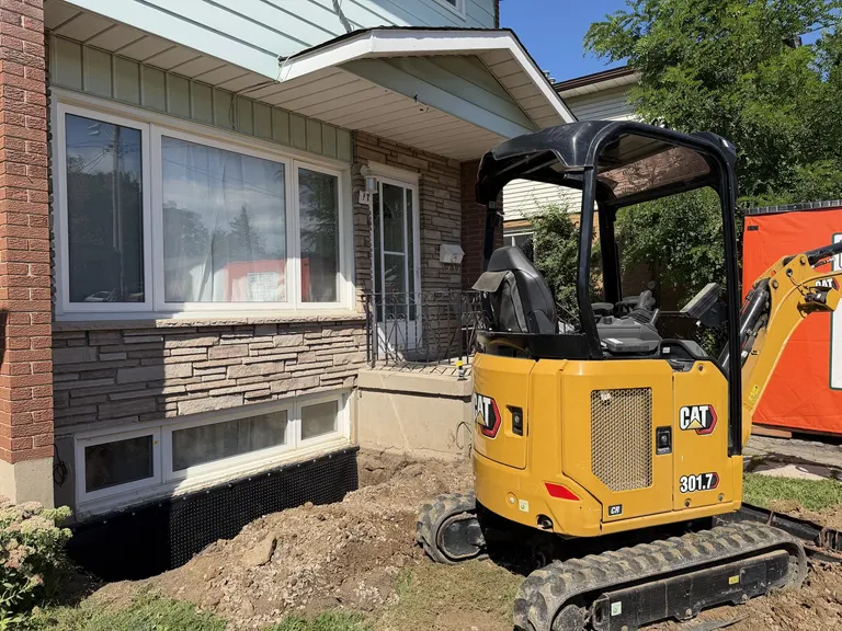 Compact excavator beside an exposed foundation wall