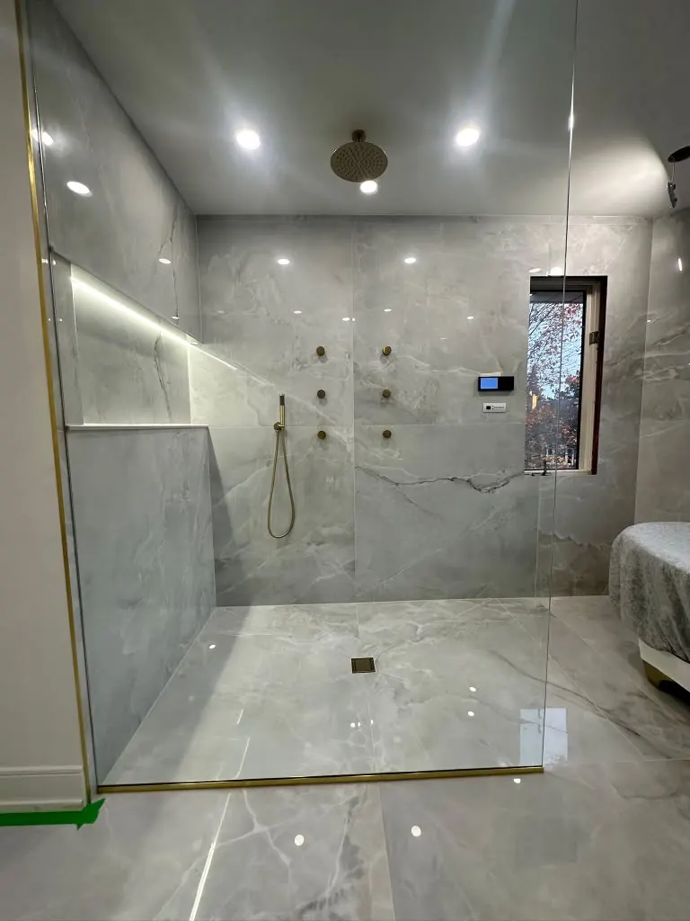 Walk-in shower with large-format grey marble porcelain tile and brushed brass fixtures