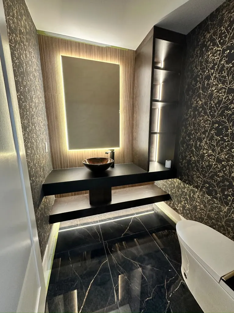 Powder room with black marble floor, gold-pattern wallpaper and backlit mirror
