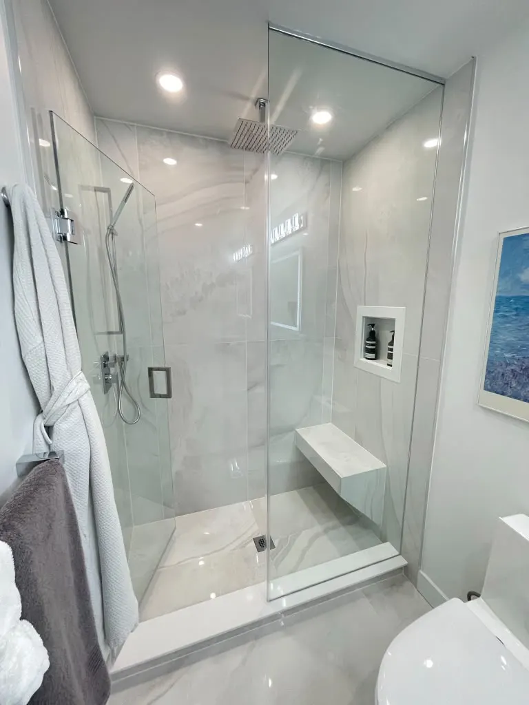 White marble tile shower with glass enclosure and bench